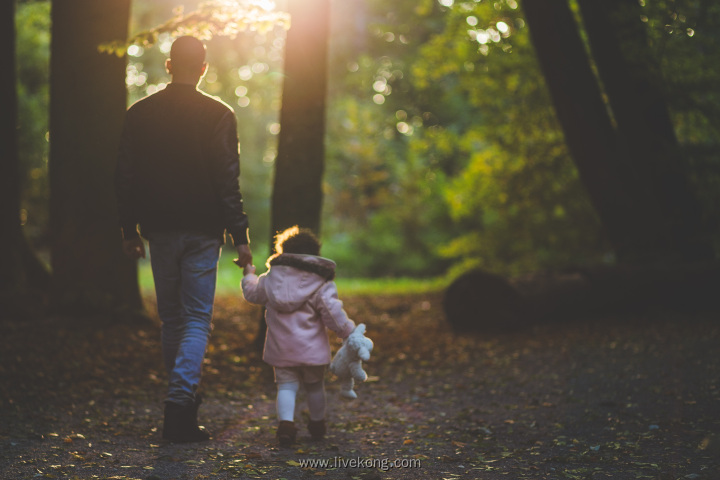 父亲牵着女儿的手在树林里走路