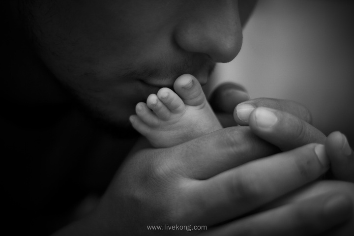 父亲握着新生儿的小脚亲吻