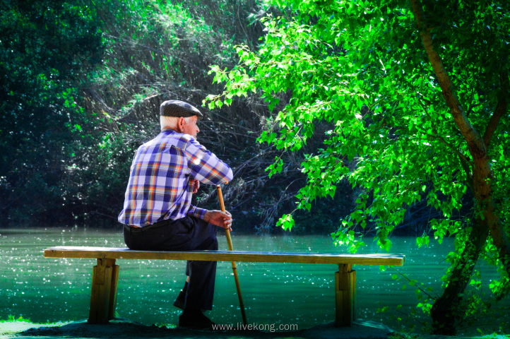 老人坐在公园小河边的长椅上休息