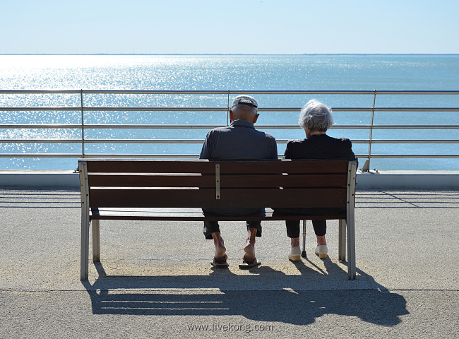 老夫妻坐在长椅上看大海风景