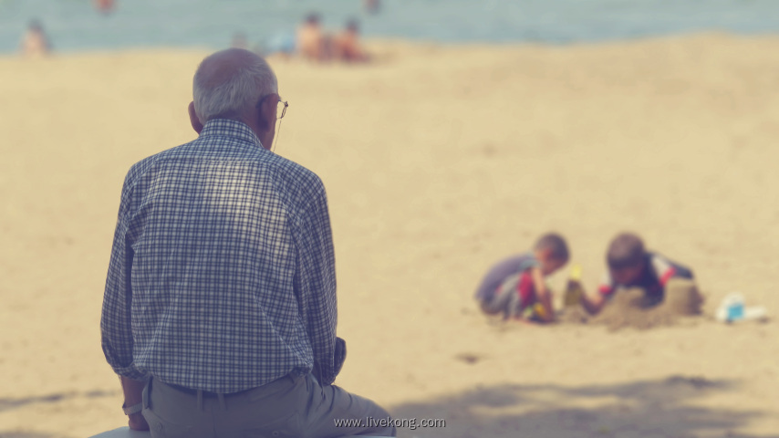 老人坐在海边看孩子们玩沙子